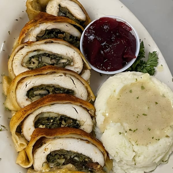 Sliced chicken roulade with mushroom stuffing, mashed potatoes with gravy, and cranberry sauce.