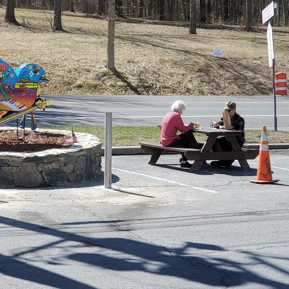 Two people eating at a picnic table outside Quickway Diner, with a colorful bird sculpture nearby.