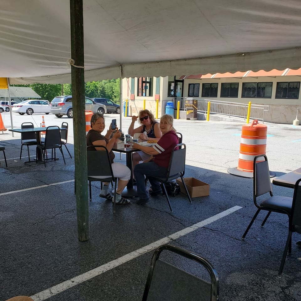 Three women enjoying a meal at an outdoor table under a white tent at Quickway Diner.