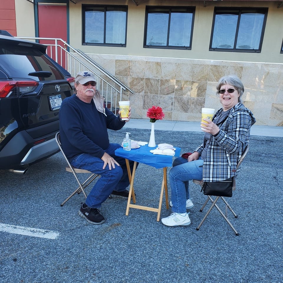 Two people enjoying coffee at a small table in the Quickway Diner parking lot.