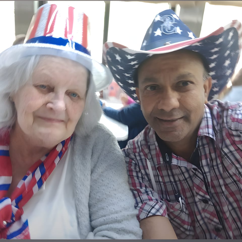 Two smiling people, an older woman and a man, wearing patriotic red, white, and blue hats.