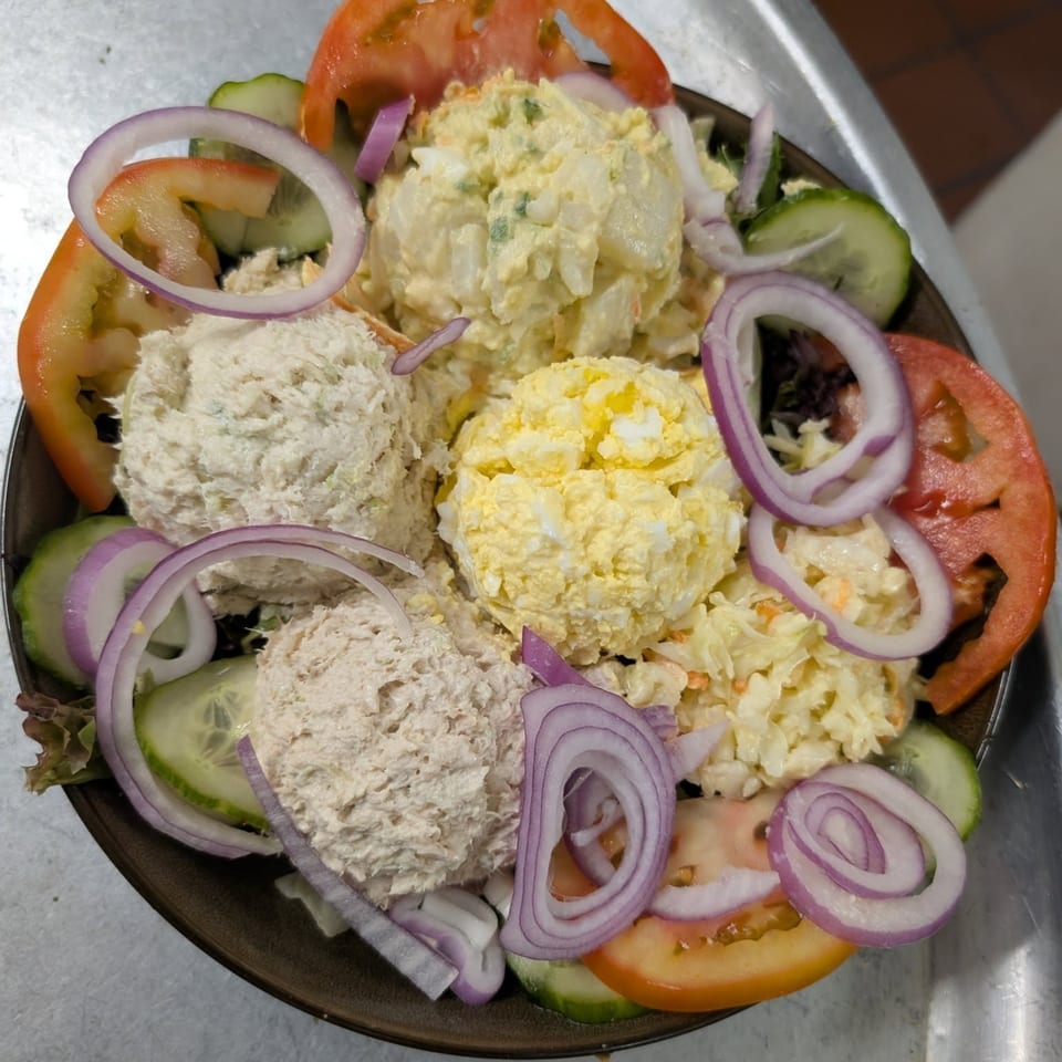 A Quickway Diner salad with scoops of tuna, egg, potato, and coleslaw, garnished with tomato, cucumber, and red onion.