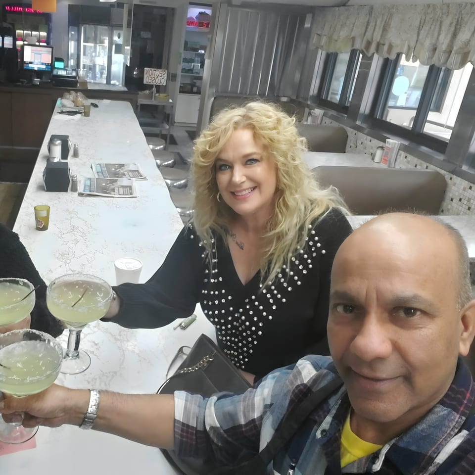 Two people smiling and toasting margaritas at the Quickway Diner counter.