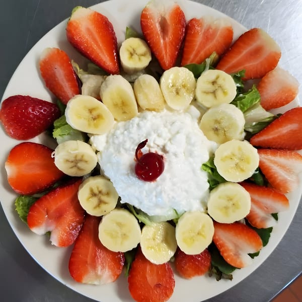 A Quickway Diner fruit plate with cottage cheese, strawberries, bananas, and a cherry on lettuce.