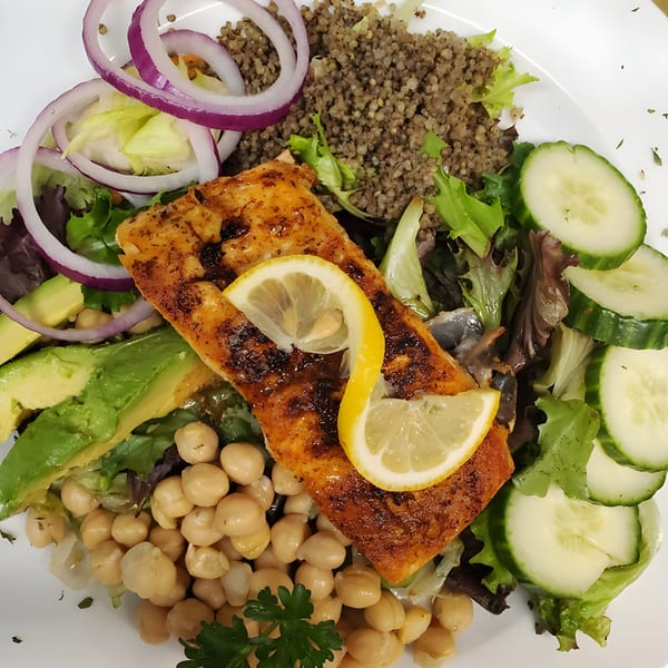 Grilled salmon with lemon slices, mixed greens, red onion, avocado, chickpeas, cucumbers, and quinoa.